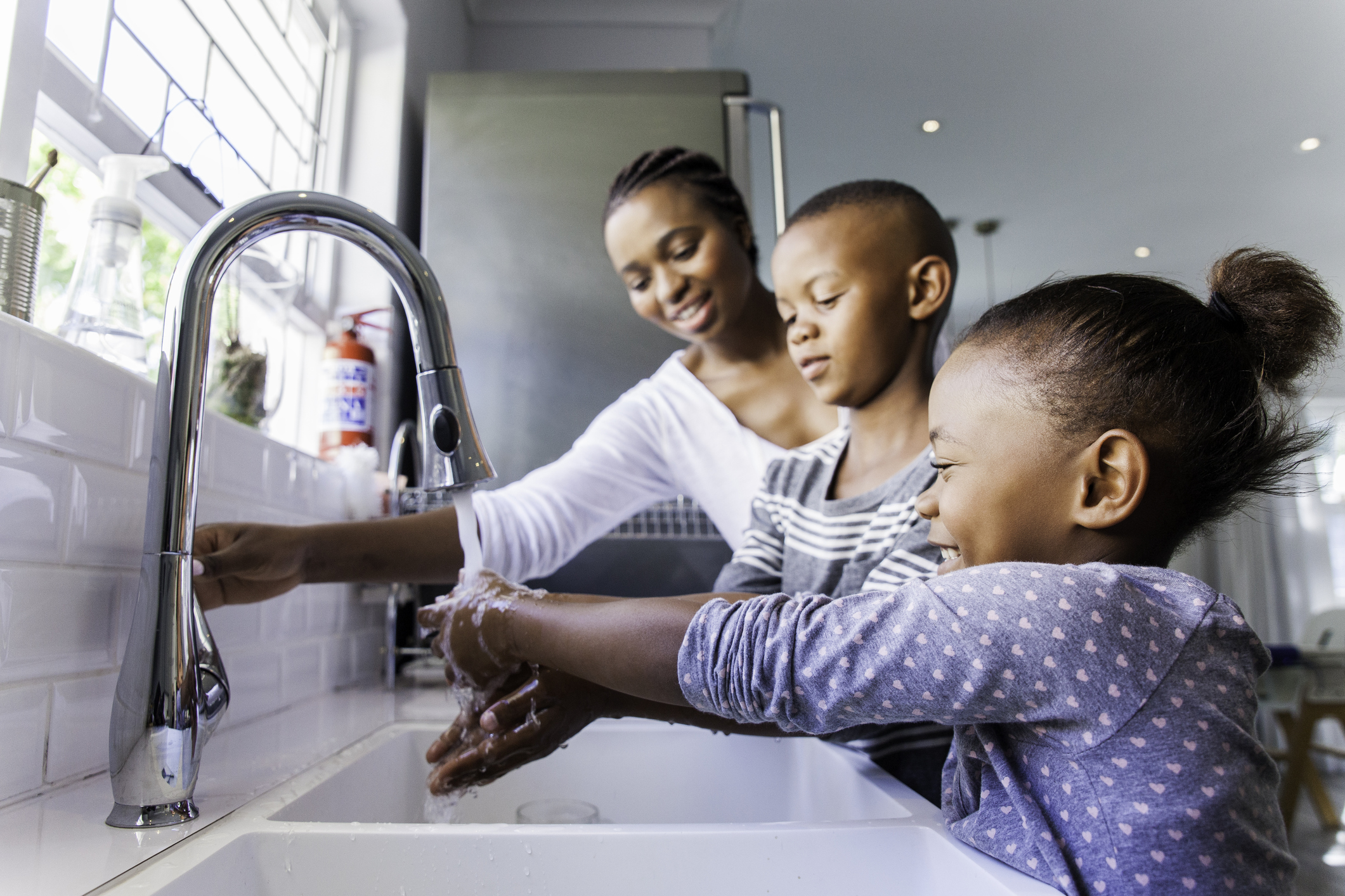 African mother opening the tap for her kids to wash their hands in the kitchen.